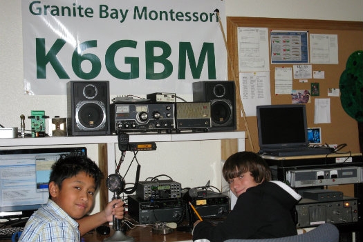 Two students are posing for a picture in front of their Montessori school station K6GBM.